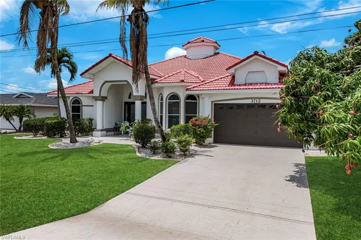 White stucco exterior with a red barrel tile roof, arched entryway, a prominent cupola, and an attached two-car garage