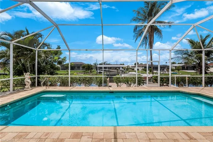 Screened pool enclosure featuring a rectangular swimming pool with integrated steps, paver decking, and metal handrails