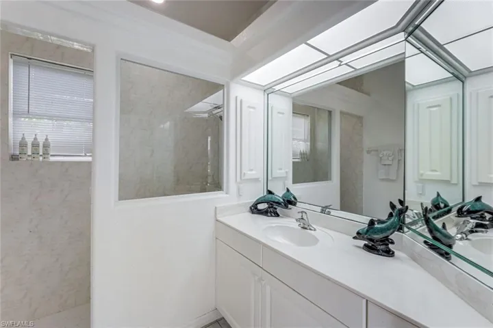 Bathroom featuring a double vanity with integrated sinks, a large mirror with integrated lighting, and a walk-in shower with a window
