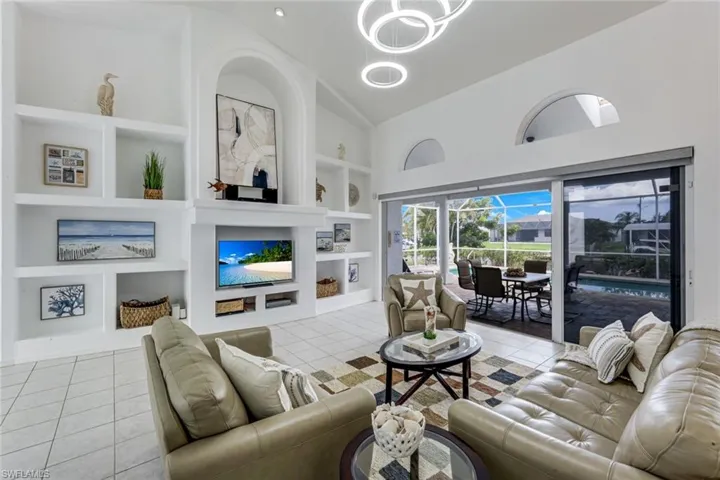 Spacious living area featuring a built-in media center with arched alcove, tile flooring, and high ceilings with contemporary lighting
