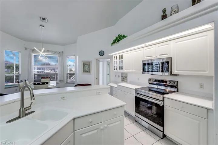 White kitchen with contemporary stainless steel appliances, white cabinetry, and white countertops