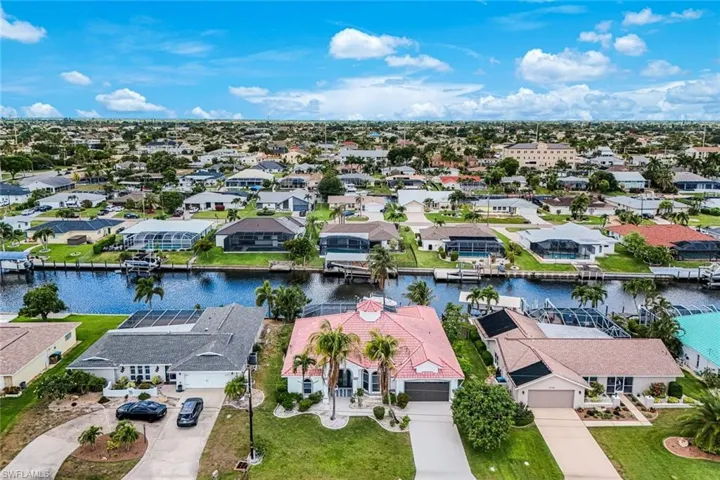 Waterfront property featuring a private boat dock, mature landscaping, a red tile roof, and an attached two-car garage