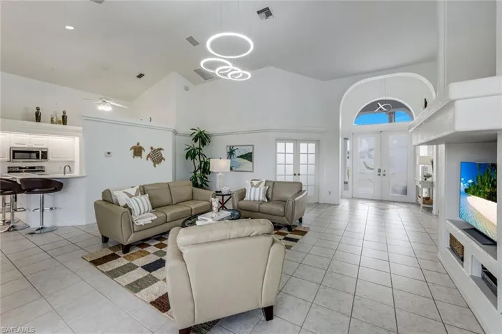 Spacious living area featuring vaulted ceilings, contemporary circular pendant lighting, and light-toned tile flooring