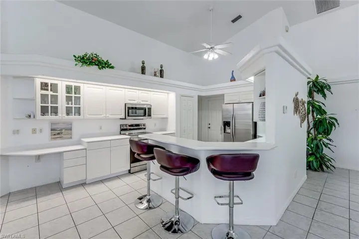 Kitchen featuring white cabinetry, stainless steel appliances, a breakfast bar, a built-in desk area, and tile flooring
