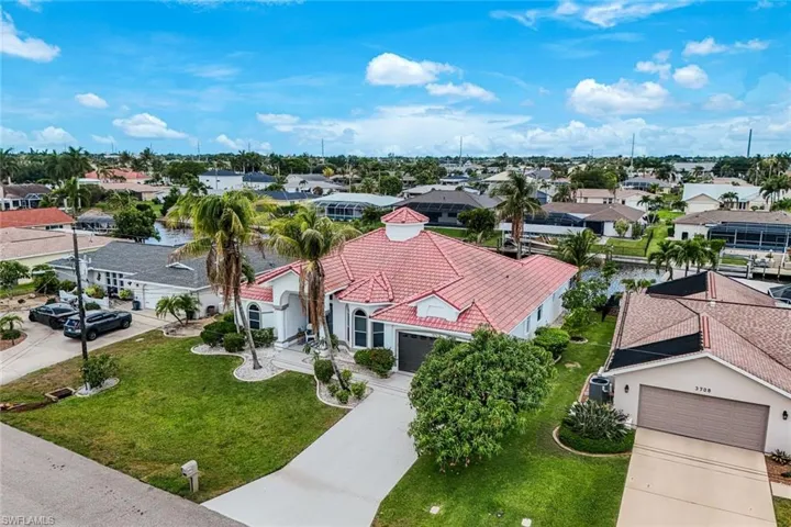 Waterfront property featuring a red tile roof, manicured landscaping, a private driveway, and a two-car garage