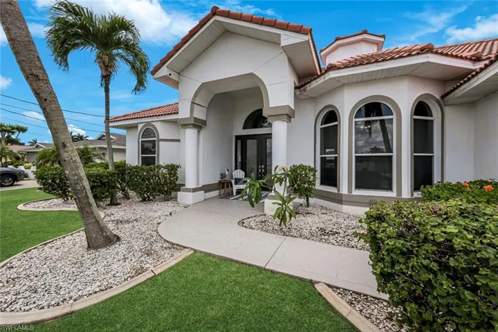Exterior featuring a white stucco facade, a red tile roof, arched windows, a curved concrete walkway, and landscaped garden beds with white stone