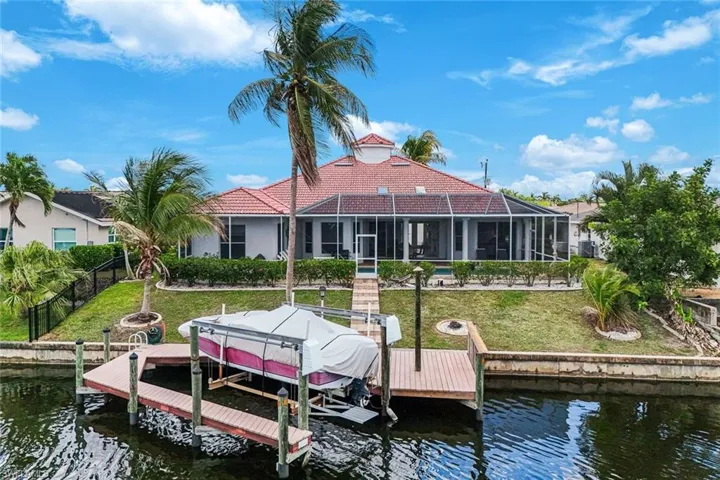 Waterfront property featuring a private dock with boat lift, screened-in lanai, tile roof, and mature palm trees