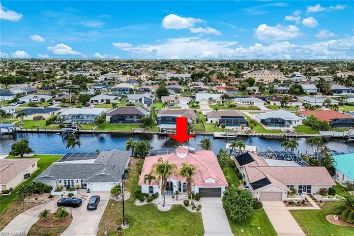 Waterfront property featuring a red tile roof, an attached garage, a paved driveway, mature palm trees, and a well-maintained lawn