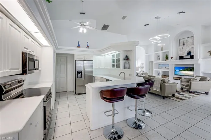 Open-concept living area featuring a kitchen with white cabinetry and stainless steel appliances, a breakfast bar, and tile flooring throughout