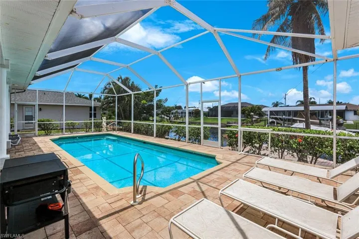 Screened-in pool area featuring a rectangular swimming pool, brick paver patio, and direct water frontage