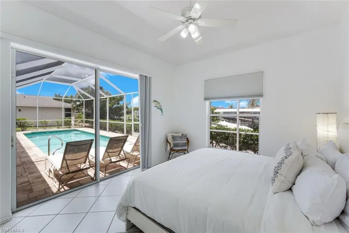 Bedroom featuring a screened-in swimming pool enclosure, large glass sliding doors, window with horizontal blinds, white ceiling fan, and tile flooring