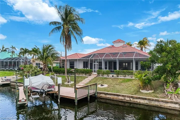 Waterfront residence featuring a screened-in lanai, tile roof, private dock, and mature palm trees