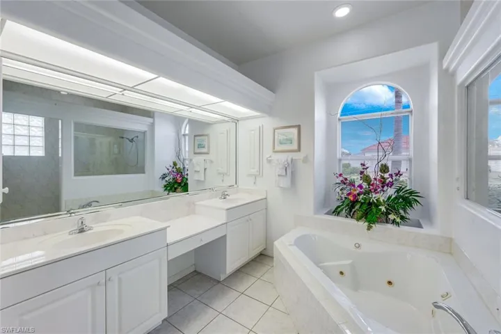 Spacious bathroom featuring a built-in jetted tub, dual vanity with undermount sinks, and a large wall-mounted mirror with integrated lighting