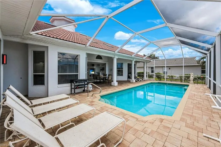 Screen-enclosed swimming pool with a paved deck, featuring a pool cage and direct access to the interior via a sliding glass door