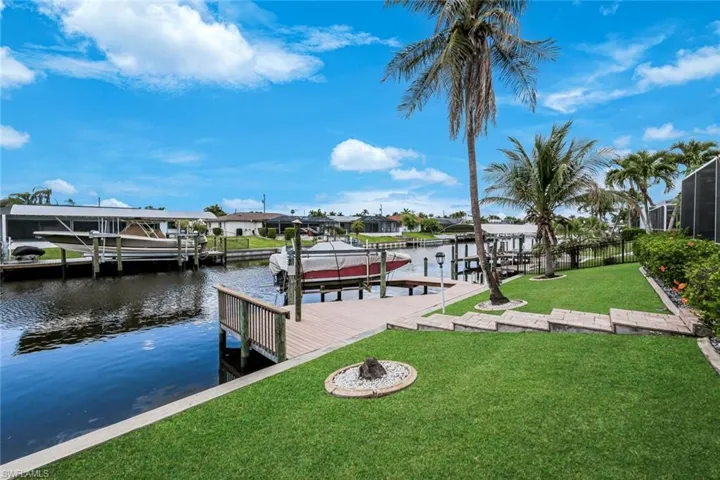 Waterfront property featuring a private boat dock, manicured lawn, and tropical landscaping