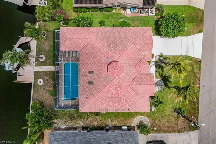 Property featuring a terra cotta tile roof, screen-enclosed pool, private boat dock with lift, and a concrete driveway