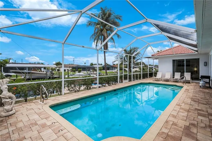 Screened-in pool area featuring a rectangular swimming pool, paver deck, and tropical landscaping