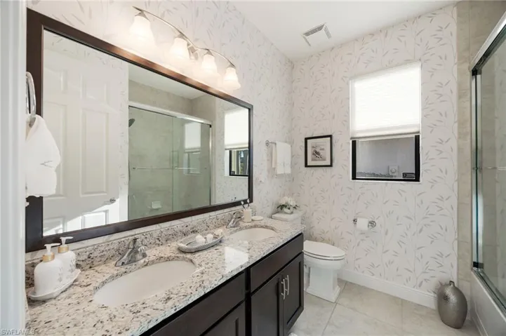 Bathroom with wallpapered walls, double vanity, light tile patterned floors, and enclosed tub / shower combo