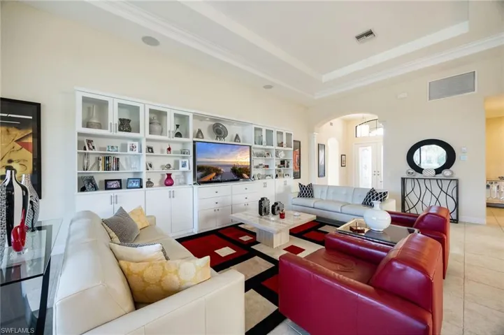 Living room featuring arched walkways, a high ceiling, tile patterned floors, a raised ceiling, and crown molding
