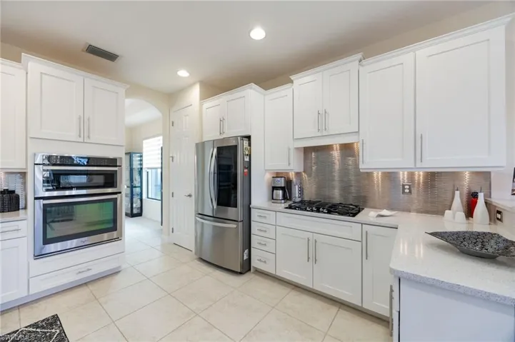 Kitchen with appliances with stainless steel finishes, white cabinetry, arched walkways, backsplash, and light stone countertops