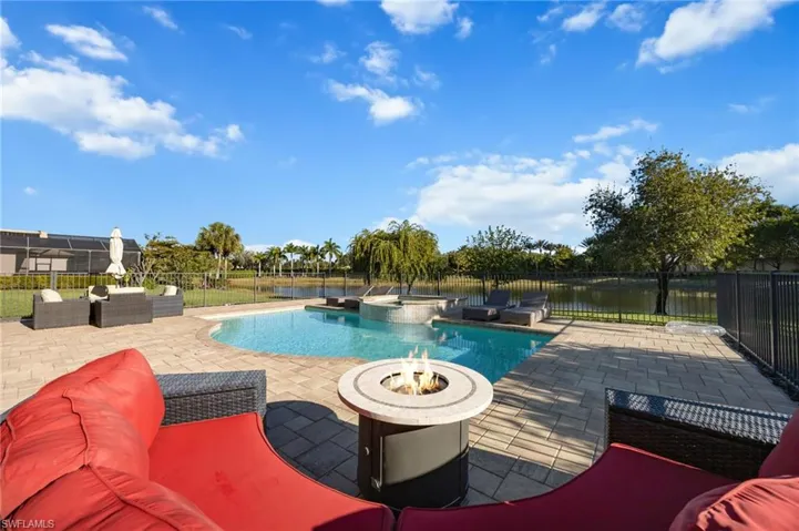 View of pool featuring an outdoor living space with a fire pit, a patio, a pool with connected hot tub, a fenced backyard, and a water view