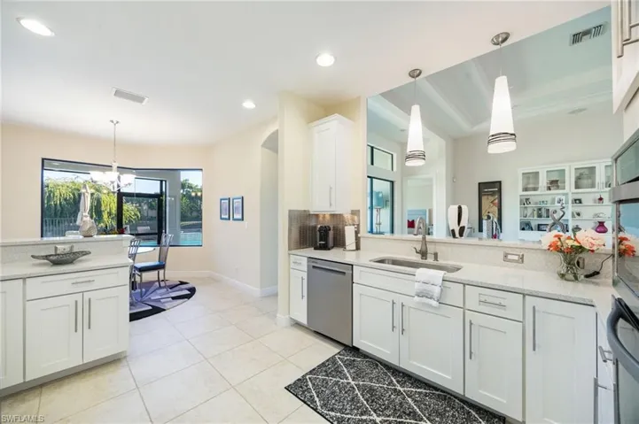 Kitchen featuring white cabinetry, pendant lighting, a chandelier, dishwasher, and light stone countertops