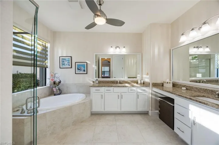 Full bath featuring a garden tub, a shower stall, two vanities, light tile patterned floors, and ceiling fan