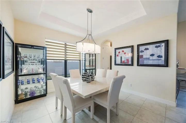 Dining room featuring a raised ceiling, light tile patterned floors, and arched walkways
