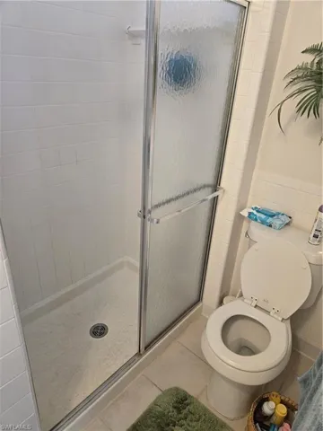 Bathroom with tile patterned floors, toilet, an enclosed shower, and tile walls