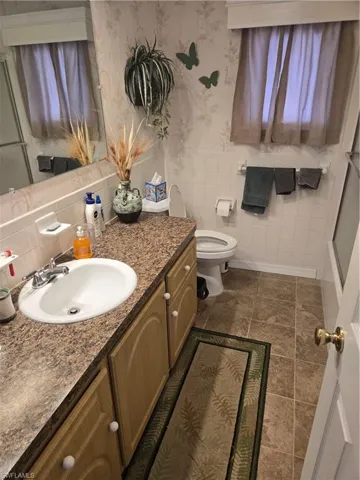 Bathroom featuring walk in shower, vanity, toilet, and tile walls