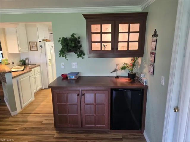 Kitchen with hardwood / wood-style floors, refrigerator, white cabinetry, white fridge with ice dispenser, and crown molding