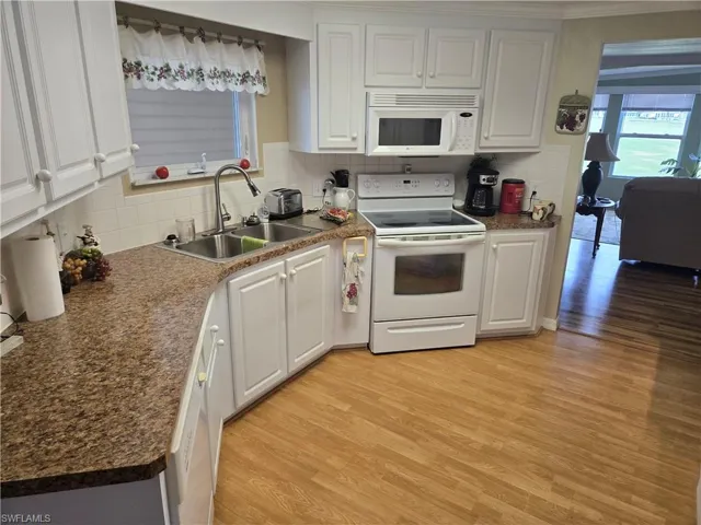 Kitchen featuring white cabinetry, white appliances, light hardwood / wood-style floors, and sink