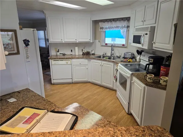 Kitchen featuring white cabinetry, sink, light wood-type flooring, decorative backsplash, and white appliances