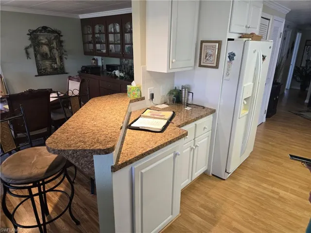 Kitchen with white cabinetry, white fridge with ice dispenser, kitchen peninsula, and a breakfast bar