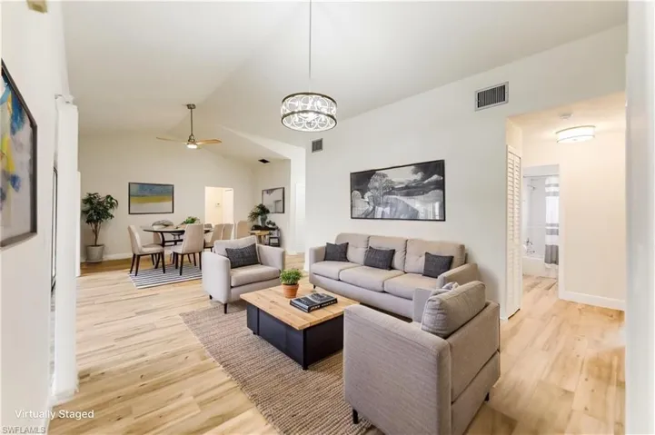 Living area featuring ceiling fan, light wood-style floors, vaulted ceiling, and a chandelier