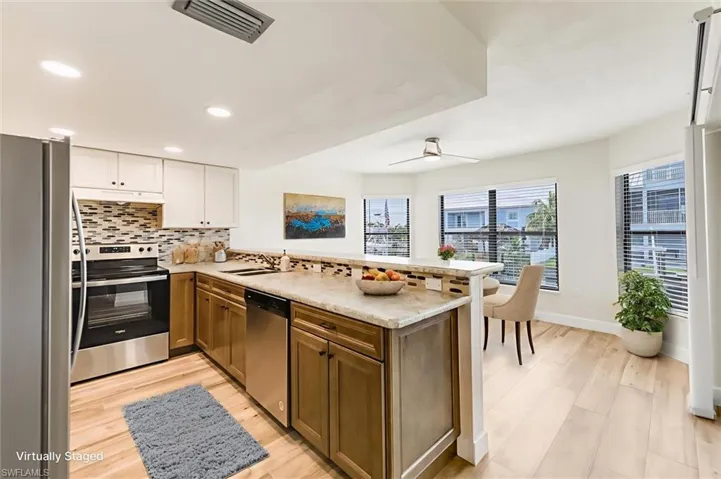 Kitchen featuring appliances with stainless steel finishes, a peninsula, tasteful backsplash, under cabinet range hood, and light wood finished floors