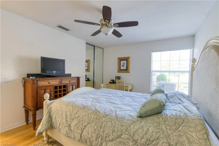 Spacious room featuring light wood-finish flooring, a large window with horizontal blinds, a ceiling fan with integrated lighting, and a mirrored closet door