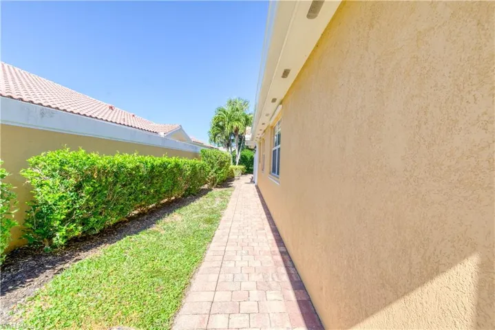 Exterior pathway featuring textured stucco siding, a brick paver walkway, and a manicured hedge