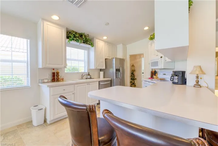 Kitchen featuring white cabinetry, light-toned countertops, stainless steel refrigerator, white microwave, and tile flooring