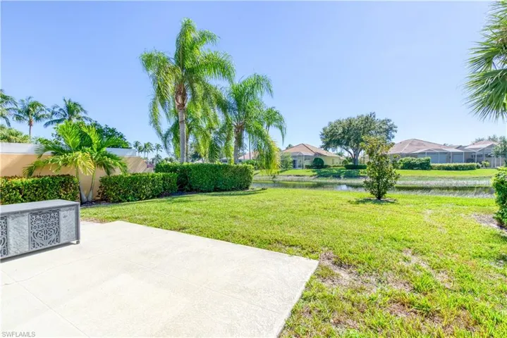 Expansive green space featuring a concrete patio, lush lawn, mature palm trees, and manicured hedges overlooking a water feature