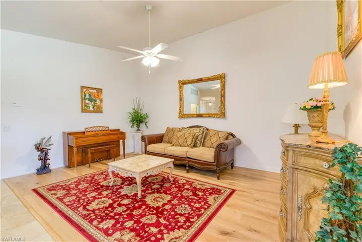 Spacious living area featuring light wood-finish flooring, a vaulted ceiling, and a ceiling fan with integrated lighting