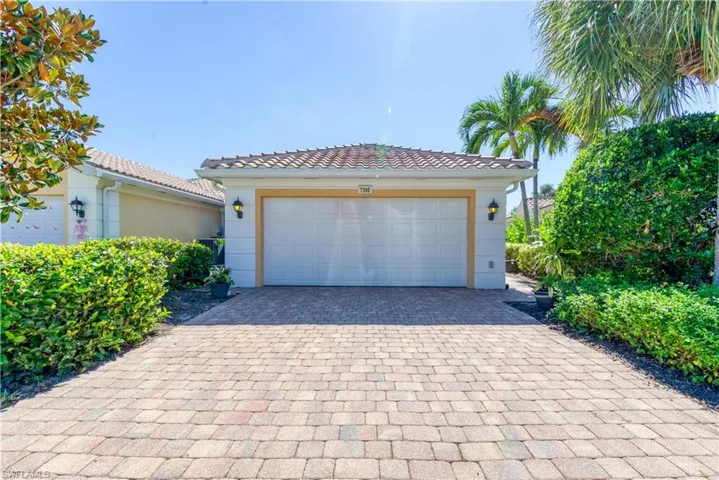 Brick paver driveway leading to a two-car garage with wall-mounted coach lights