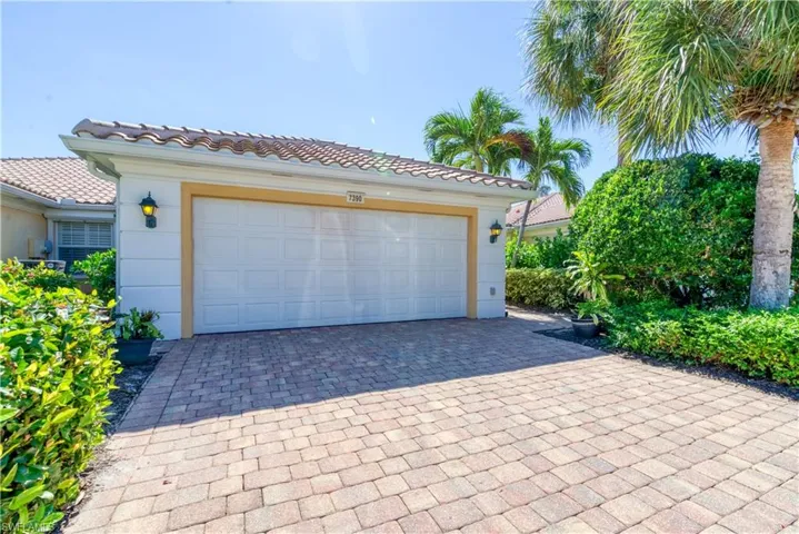Paver driveway leading to a two-car garage with exterior wall sconces