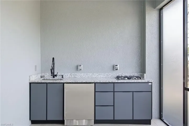 Indoor wet bar with light stone countertops, stainless steel appliances, a textured wall, gray cabinets, and light tile patterned flooring