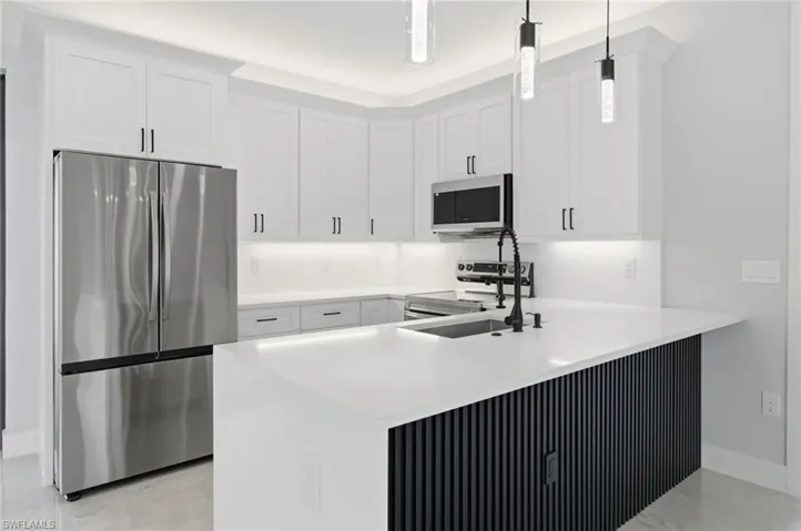 Kitchen featuring stainless steel appliances, white cabinetry, light stone countertops, and a peninsula