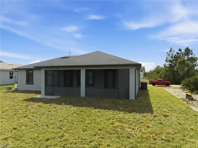 Rear view of property featuring a lawn, roof with shingles, stucco siding, and a sunroom