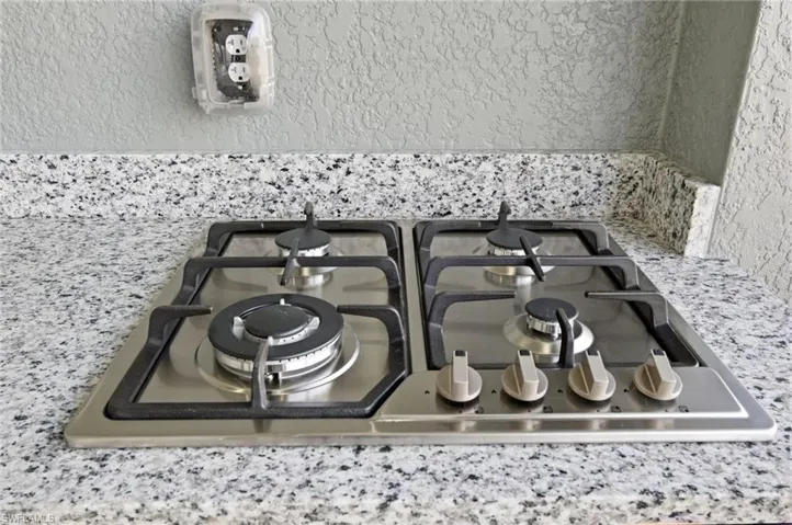 Kitchen view of stainless steel gas cooktop, light stone countertops, and a textured wall