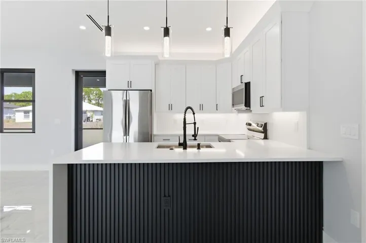 Kitchen featuring stainless steel appliances, light stone counters, white cabinets, and a peninsula
