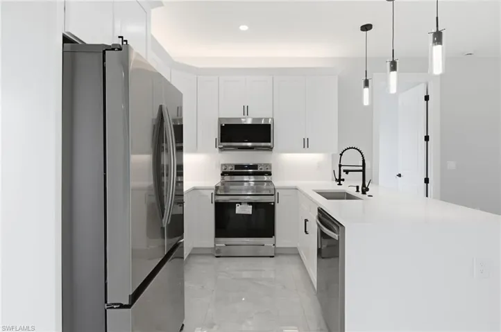 Kitchen with stainless steel appliances, a peninsula, light stone countertops, white cabinets, and hanging light fixtures