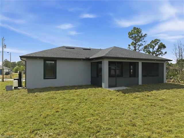 Rear view of property featuring a sunroom, a lawn, stucco siding, and roof with shingles